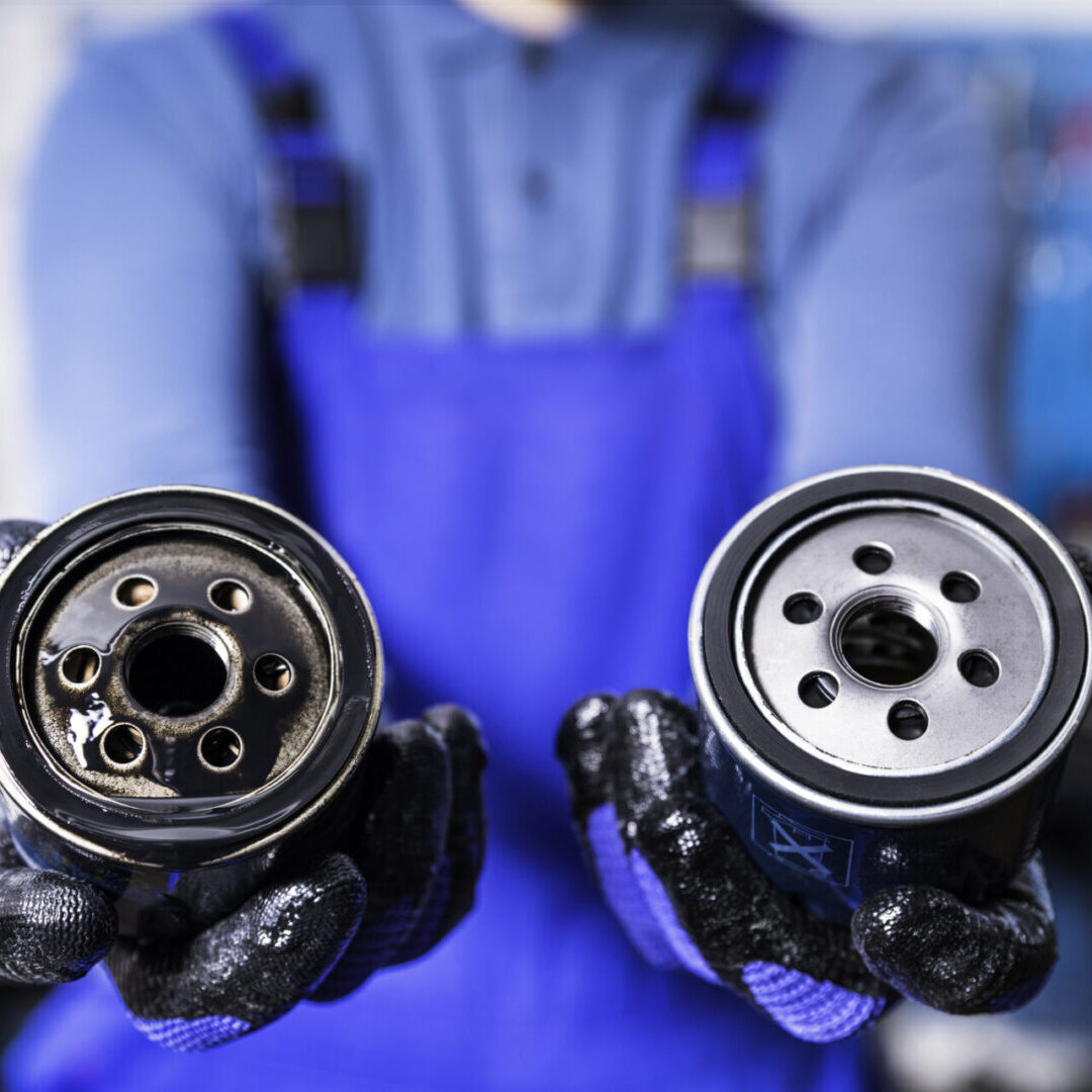 Technician holding automotive oil filters with gloved hands.